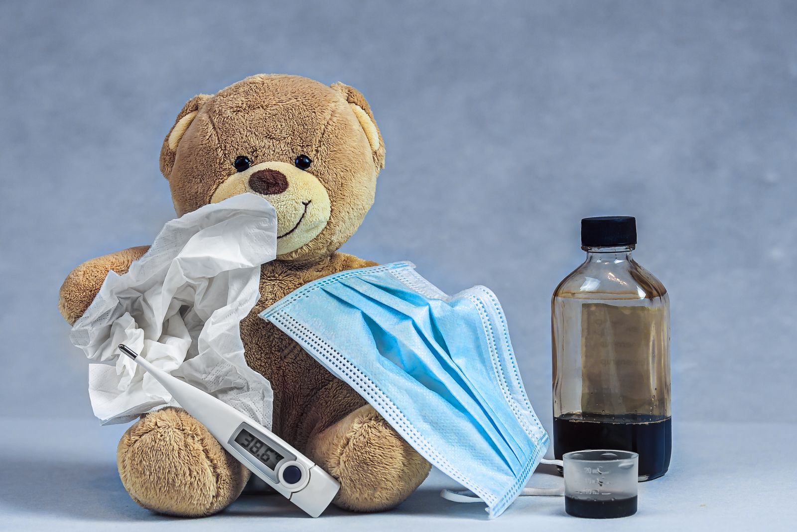 Ourson en peluche avec un thermomètre, un masque et du sirop contre la toux